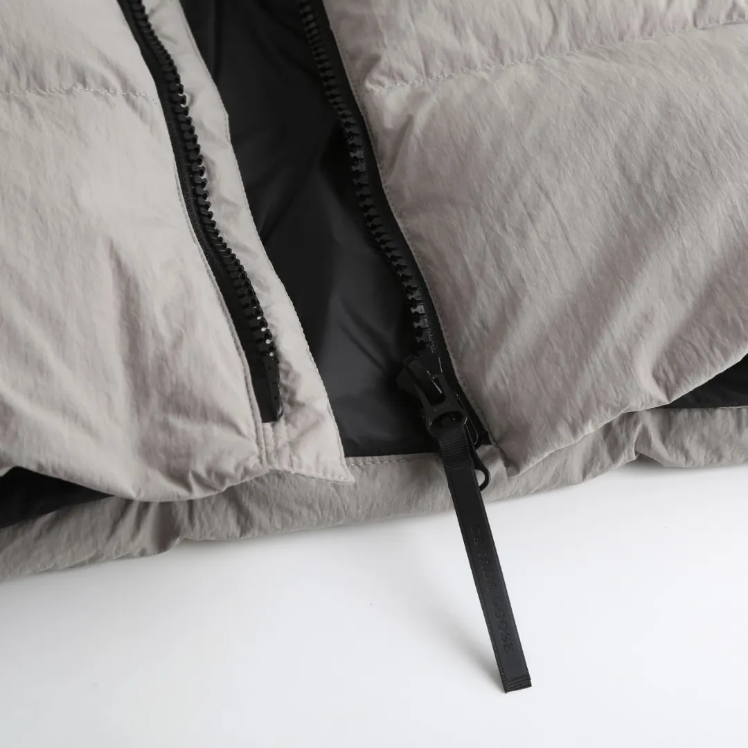 P980 Canada Goose hooded down jacket Fabric selection: Weaved with 400T high-count yarn. After special water-repellent treatment, the surface forms a lotus leaf effect - raindrops will slide down in beads, and snow particles will fall off when touched. The tear resistance reaches 200N (approximately 20kg load-bearing), the light gray matte texture breaks the stereotype of "outdoor clothing = hardcore", and the soft luster presents a high-end matte effect under urban neon lights, seamlessly switching scenes from ski resorts to CBD office buildings.  Process 1: Use polyester woven ribbons as the base, and use high-precision computer embroidery to decorate the brand letters on the ribbons. The edges of the pattern are clear, the stitches are fine and even, and multiple layers of embroidery threads are stacked to enhance the three-dimensional effect.  Process 2: Precision thread reinforcement to prevent velvet drilling and ensure that the fluffy and resilient elasticity lasts as new.  Details: The embedded cuffs are three-dimensionally woven to form a "wavy" elastic structure, forming natural folds when fitting the wrist, increasing the contact area with the skin, thus improving the windproof effect. At the same time, micro-velvet treatment is added to the inside of the cuffs, which feels like a second layer of skin and avoids friction on the skin from metal zippers or hard fabrics.  90 national standard high-quality white duck down: selected high-loft down, weighing 240g, light and warm, with excellent temperature locking performance and good resilience.  Accessories: 1:1 customized armband, 1:1 customized zipper pendant, 1:1 customized elastic buckle, etc. SIZE: S M L XL